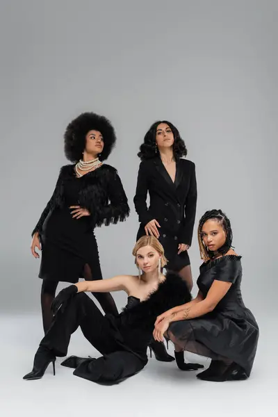 Diverso grupo de sofisticadas mujeres multiétnicas en traje negro sobre fondo gris, sesión de fotos de moda - foto de stock