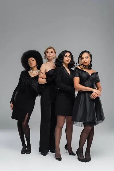 In voller Länge anmutige multikulturelle Freundinnen in schwarzer eleganter Kleidung stehen auf grau — Stockfoto