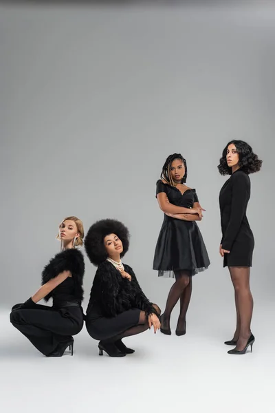 Charmante multikulturelle Models posieren in schwarzer Kleidung vor grauem Hintergrund, stilvolle Freundinnen — Stockfoto