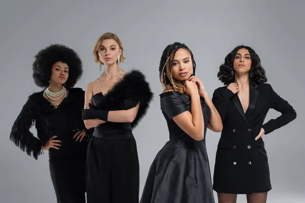 Diverse multirassische Freundinnen in schwarzer stylischer Kleidung schauen in die Kamera auf grau, High Fashion — Stockfoto
