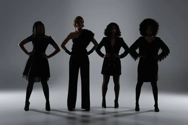 Dunkle Silhouetten von eleganten multirassischen Freundinnen in Schwarz, die mit Händen auf Hüften auf grau posieren — Stockfoto