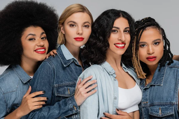 Retrato de grupo de namoradas multiétnicas em denim desgaste olhando para a câmera em cinza, beleza diversificada — Fotografia de Stock