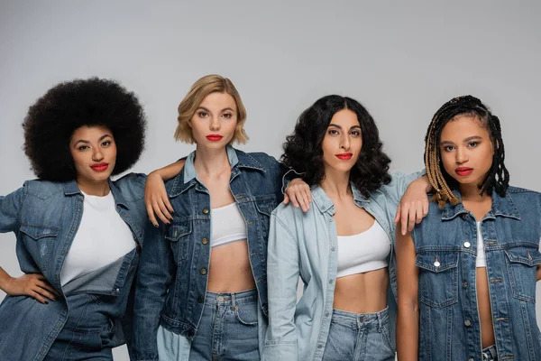 Group portrait of trendy multicultural girlfriends in blue denim wear posing on grey backdrop — Stock Photo