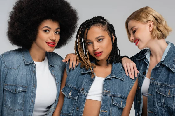 Diverse and charming multiracial girlfriends in blue denim attire posing on grey, modern fashion — Stock Photo