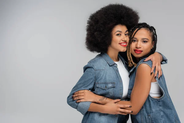 Gaie et branchée copines afro-américaines embrassant sur fond gris, mode denim — Photo de stock