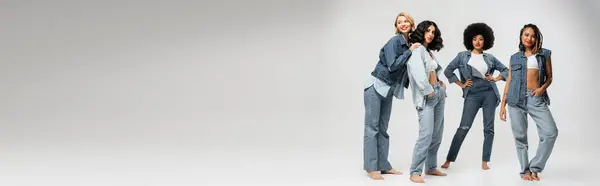 Modische multirassische Freundinnen in blauer Jeans stehen barfuß auf grauem, waagerechtem Banner — Stockfoto
