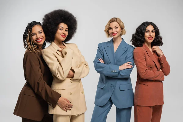 Group of trendy multiethnic girlfriends in multicolored suits smiling at camera on grey, diversity — Stock Photo
