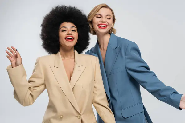 Joyful and fashionable multiracial women posing in colorful suits on grey backdrop, diverse beauty — Stock Photo