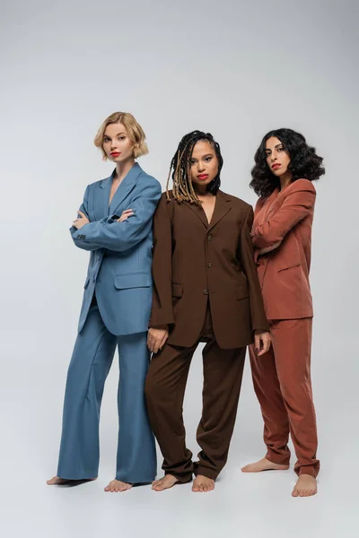 African american woman looking at camera near barefoot multiracial girlfriends in colorful suits — Stock Photo