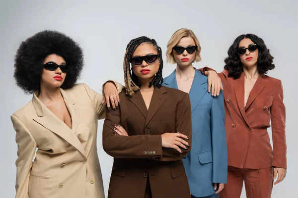 Diversidade e confiança, namoradas multirraciais em óculos escuros e ternos coloridos em cinza — Fotografia de Stock