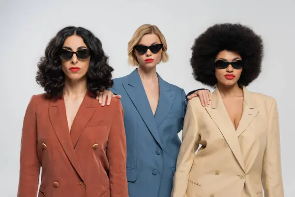 Diversidad y estilo, mujeres multiculturales en trajes coloridos de moda y gafas de sol oscuras en gris — Stock Photo