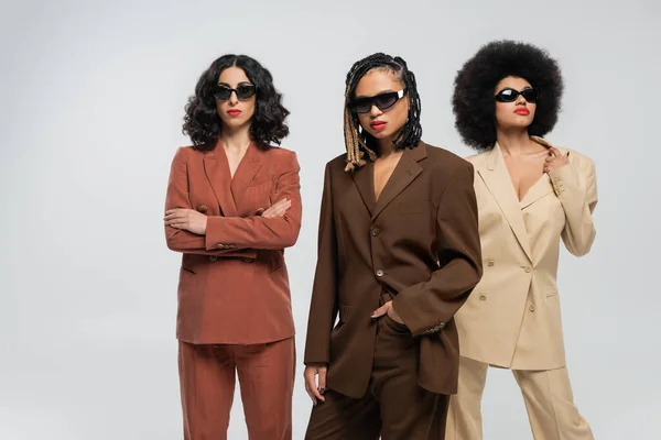 African american woman in sunglasses with hand in pocket near multiracial models in colorful suits — Stock Photo