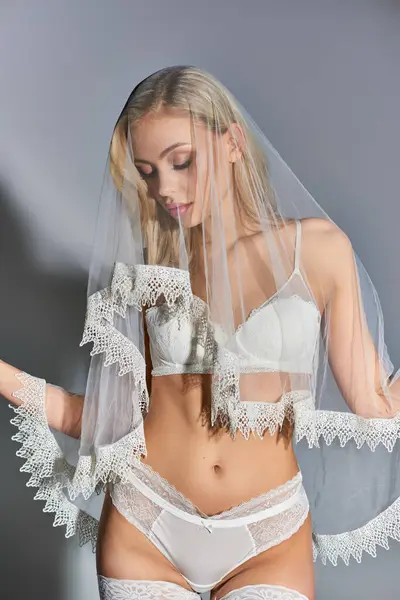 Hot young female model in white erotic lingerie with veil posing alluringly on gray background — Stock Photo