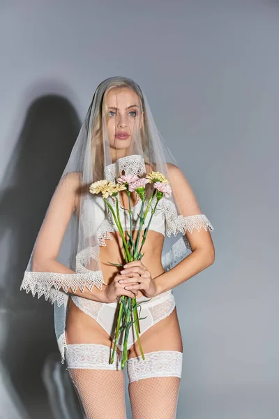 Atraente jovem modelo feminino em lingerie branca e véu posando com buquê de flores nas mãos — Fotografia de Stock