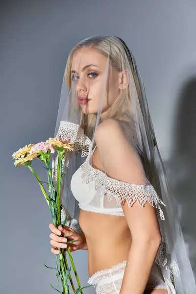 Tiro vertical de mujer joven sexy en lencería blanca posando con ramo de flores y mirando a la cámara - foto de stock
