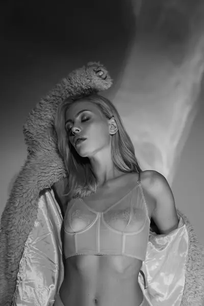 Black and white shot of alluring young woman posing in sexy lingerie with faux fur with closed eyes — Stock Photo