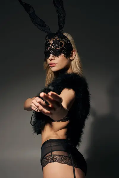 Tiro vertical de la mujer sexy en máscara de conejo y piel sintética posando con bdsm látigo y mirando a la cámara - foto de stock
