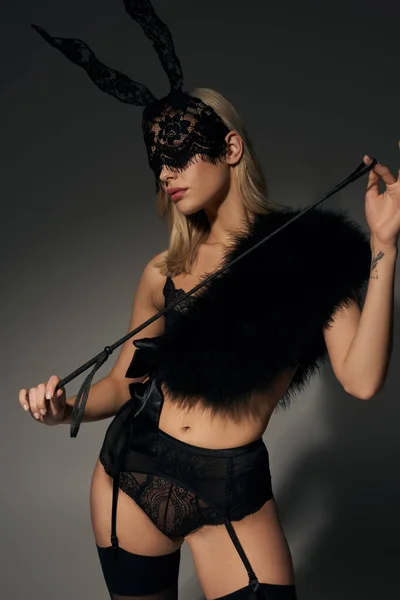 Atraente mulher sexy no coelho máscara e rendas lingerie posando com bdsm chicote e olhando para longe — Fotografia de Stock