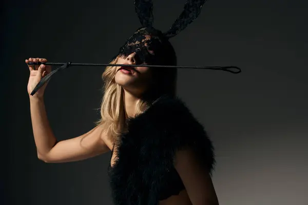 Attraktive junge Frau mit blonden Haaren in Hasenmaske posiert mit BDSM-Peitsche und blickt in die Kamera — Stockfoto