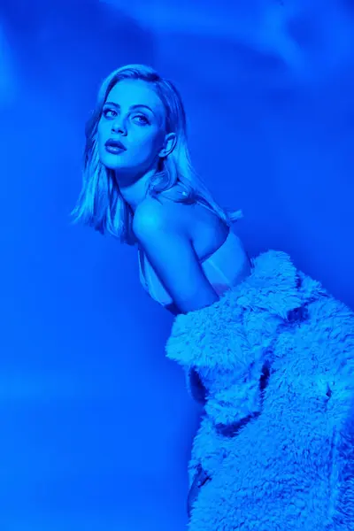 Attraente donna sexy in abbigliamento seducente piegando leggermente il suo corpo e cercando modo, luci blu — Foto stock