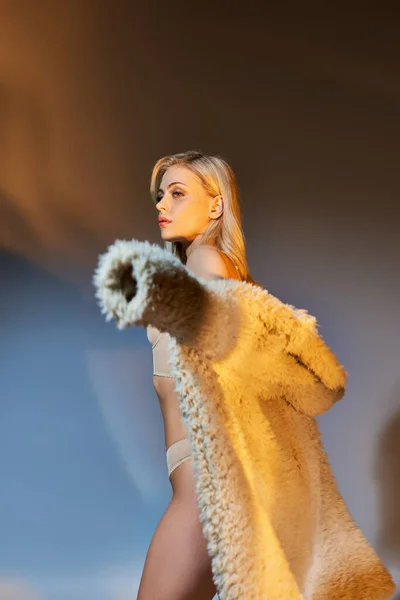 Colpo verticale di sexy giovane donna in lingerie mettere il suo cappotto di pelliccia sintetica circondato da luci — Foto stock