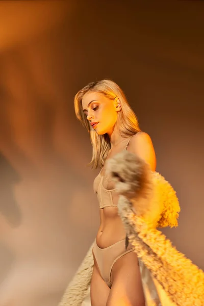 Colpo verticale di calda donna bionda in lingerie sexy pizzo ed eco pelliccia in posa circondata da luci — Foto stock