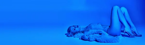 Привлекательная женщина в эротическом белье и искусственном мехе, лежащих на полу в окружении голубых огней, баннер — стоковое фото