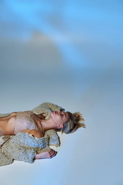 Colpo verticale di caldo bionda modello femminile in lingerie sexy beige e pelliccia sintetica sdraiato sul pavimento — Foto stock