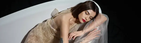 High angle view of graceful young woman in transparent dress while lying on bathtub on black, banner — Stock Photo