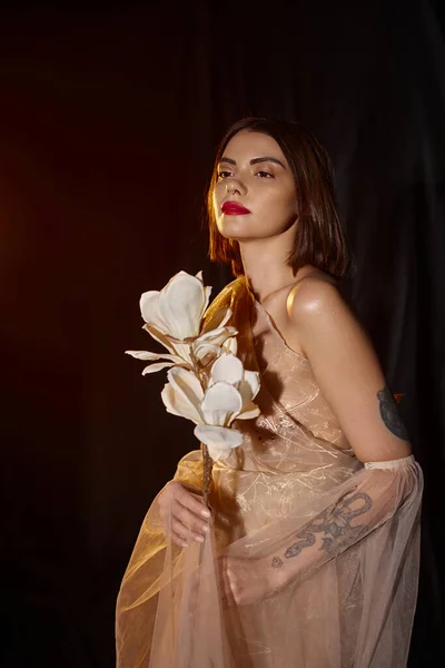 Giovane e graziosa donna in abito trasparente con fiore bianco in fiore su sfondo nero — Foto stock