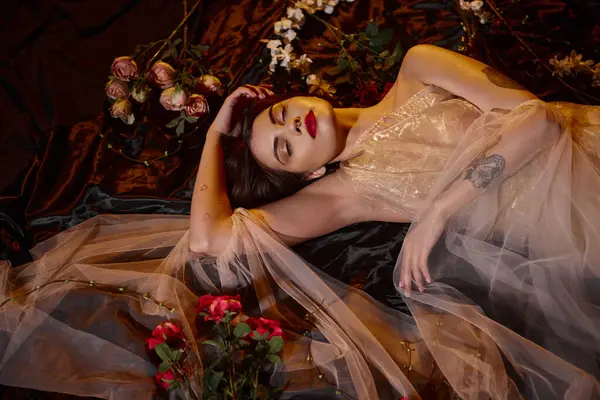 Чарівна татуйована молода жінка в романтичній прозорій сукні, що лежить серед квітів — стокове фото