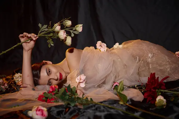 Чувственная молодая женщина в романтическом прозрачном платье, лежащем среди красивых цветущих цветов — стоковое фото
