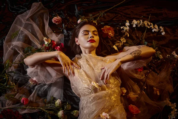 Eleganza femminile, giovane donna tatuata in romantico abito trasparente sdraiata tra bellissimi fiori — Foto stock