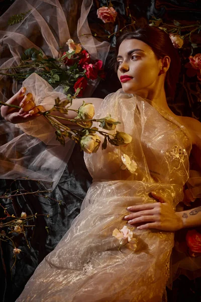 Feminine elegance, attractive woman in romantic transparent dress lying among beautiful flowers — Stock Photo