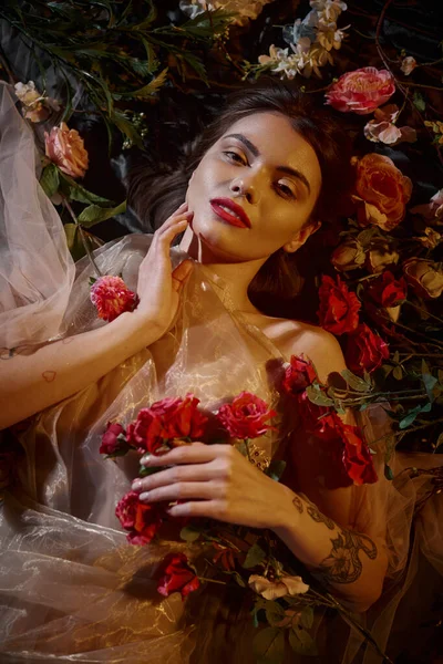 Чуттєва жінка в романтичній прозорій сукні, що лежить серед красивих квітів і дивиться на камеру — стокове фото