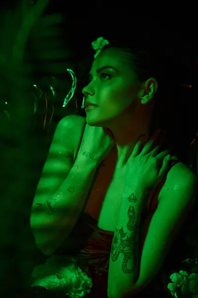Зеленый свет, привлекательная молодая женщина с мокрыми волосами, позирующая среди цветов, отводя взгляд — стоковое фото