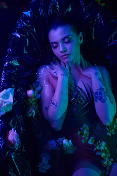 Luz azul, mujer atractiva y joven con los ojos cerrados acostado en la bañera con flores florecientes - foto de stock
