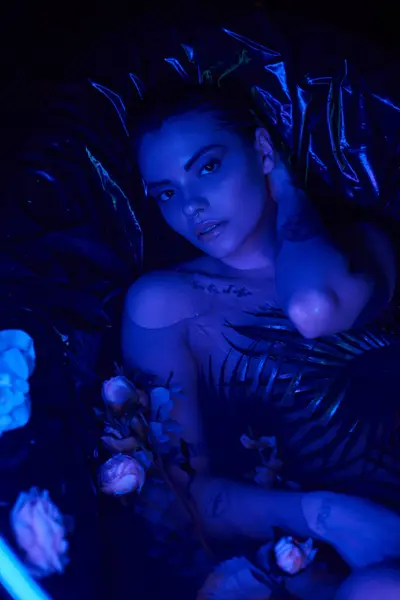 Lumière bleue, attrayant et jeune femme couchée dans la baignoire avec des fleurs en fleurs, corps mouillé — Photo de stock