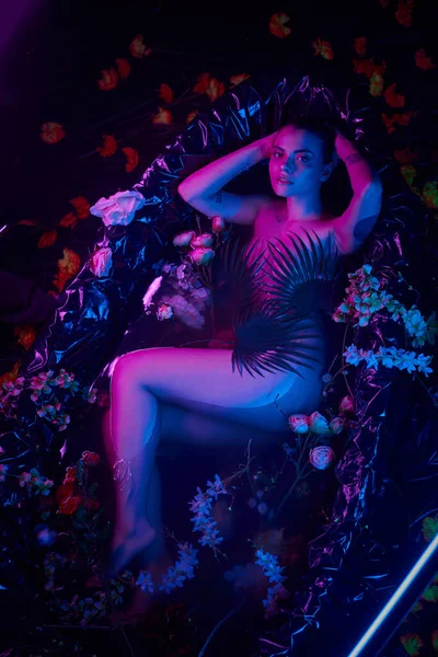 Фіолетове і блакитне світло, приваблива і молода жінка лежить у ванні з квітами — стокове фото