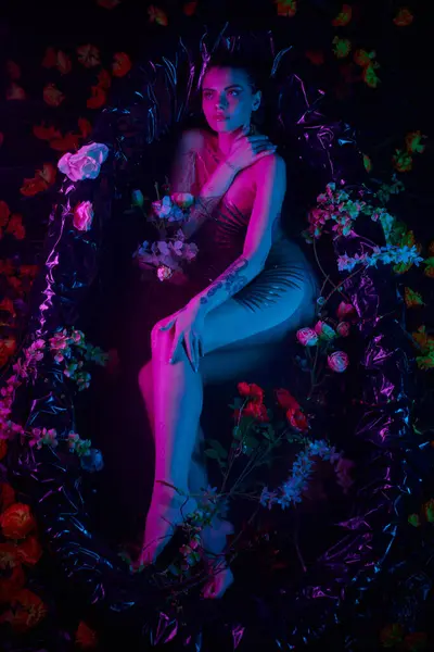 Tiro de moda, encantadora mujer acostada entre hojas de palma y flores en bañera, luces azules y púrpuras - foto de stock
