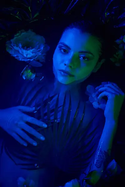 Weibliche Schönheit, charmante junge Frau, die zwischen Palmenblättern und Blüten im Wasser liegt, blaues Licht — Stockfoto