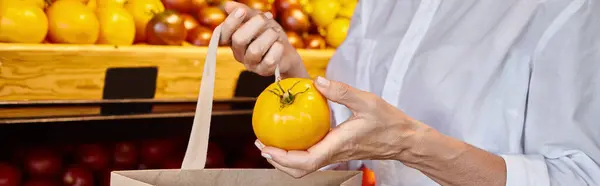 Vista recortada de la mujer poniendo tomate amarillo en la bolsa de compras, mientras que en la tienda de comestibles, pancarta - foto de stock