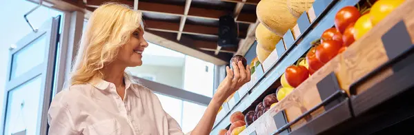 Donna matura in abito casual con carrello della spesa in mano scegliendo frutta al negozio di alimentari, banner — Foto stock
