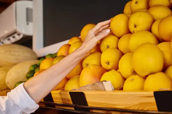 Vista recortada de la mano de la mujer madura alegre recogiendo naranjas en la tienda de comestibles, mercado de agricultores - foto de stock