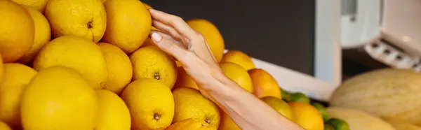 Vista recortada de la mano de la mujer alegre madura recogiendo naranjas orgánicas en la tienda de comestibles, pancarta - foto de stock
