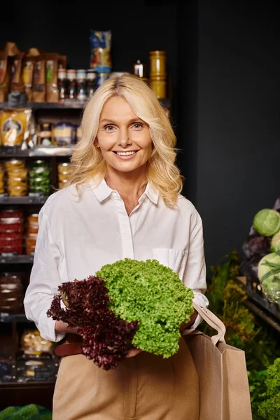 Attraktive blonde Frau im lässigen Outfit mit rotem und grünem Salat und lächelnd in die Kamera — Stockfoto