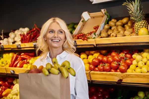 Cheerful senior female customer posing with shopping bag full of fresh fruits and looking away — Stock Photo