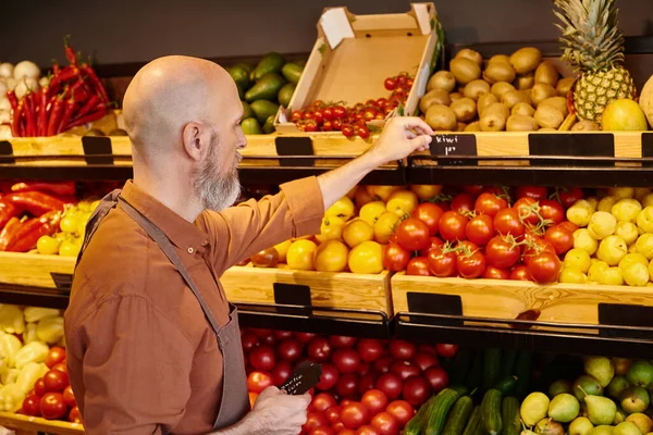 Bearded mature salesman putting price tags on vibrant fruits and vegetables at grocery store — Stock Photo