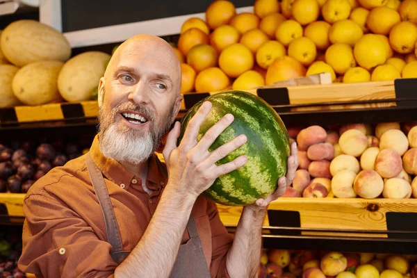 Fröhlicher bärtiger Verkäufer posiert mit glücklich mit Wassermelone am Kopf und lächelt freudig — Stockfoto