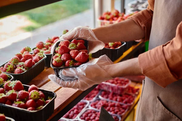 Vista ritagliata del venditore maturo che tiene in mano il pacchetto di fragole fresche e vivaci nel negozio di alimentari — Foto stock